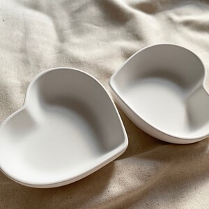 Puede incluir: Dos platos de cer&aacute;mica blanca en forma de coraz&oacute;n. Los platos son lisos y tienen un acabado brillante.