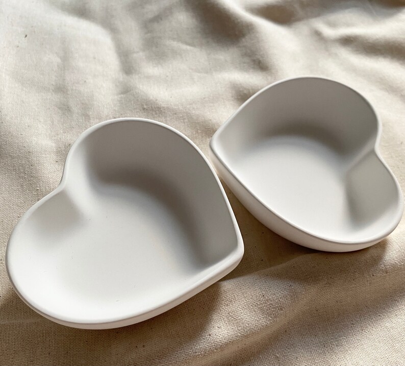 Puede incluir: Dos platos de cer&aacute;mica blanca en forma de coraz&oacute;n. Los platos son lisos y tienen un acabado brillante.