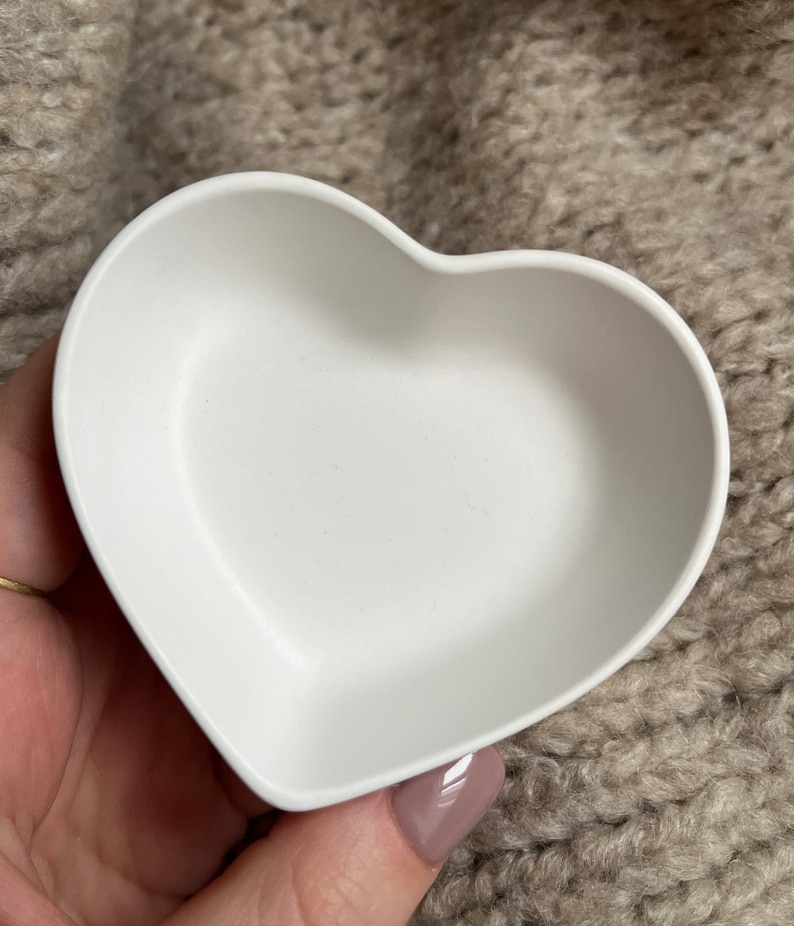 Puede incluir: Un plato blanco en forma de coraz&oacute;n hecho de silicona. El plato est&aacute; vac&iacute;o y est&aacute; siendo sostenido por una mano.