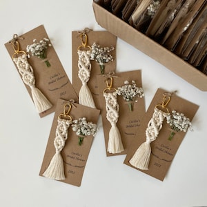 Macrame key chain knitted with cotton rope is attached to a personalized kraft card. There are white flowers on the card.