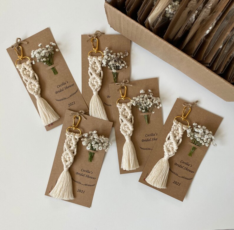 Macrame key chain knitted with cotton rope is attached to a personalized kraft card. There are white flowers on the card.