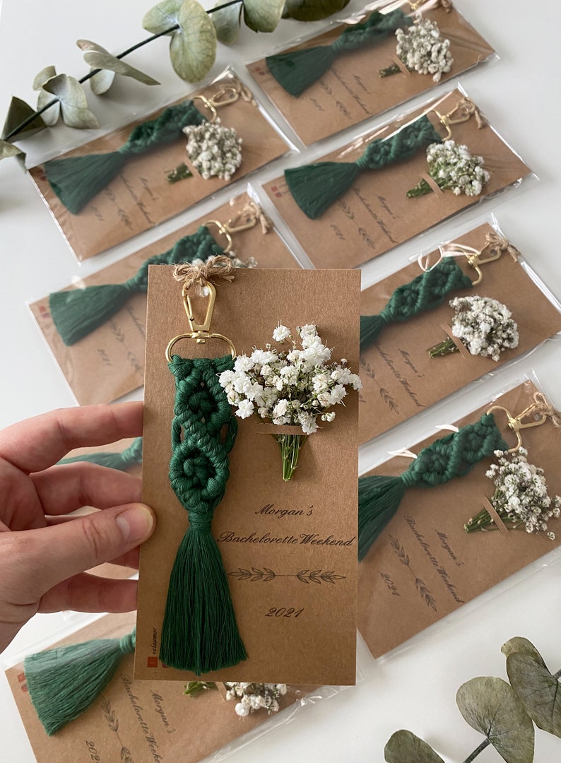 Macrame key chain knitted with cotton rope is attached to a personalized kraft card. There are white flowers on the card.
