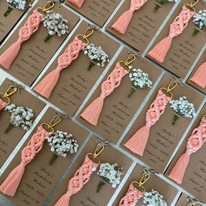 Macrame key chain knitted with cotton rope is attached to a personalized kraft card. There are white flowers on the card.