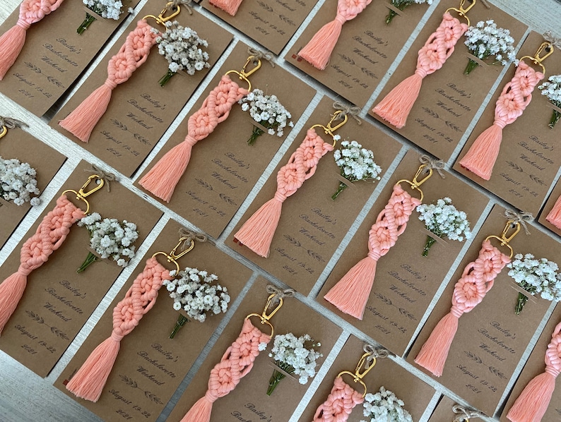 Macrame key chain knitted with cotton rope is attached to a personalized kraft card. There are white flowers on the card.