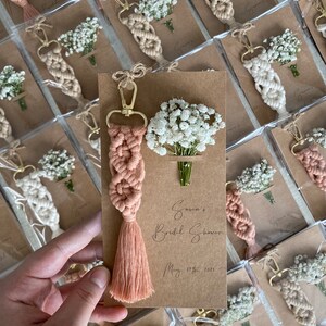 Macrame key chain knitted with cotton rope is attached to a personalized kraft card. There are white flowers on the card.