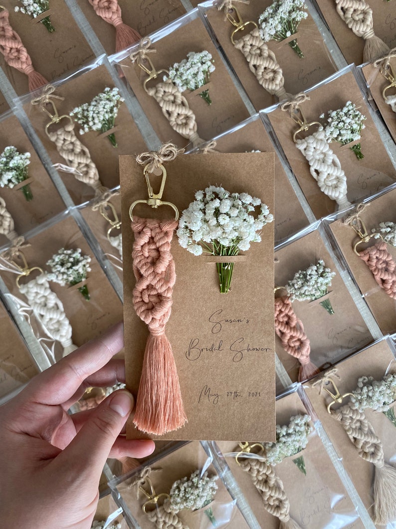 Macrame key chain knitted with cotton rope is attached to a personalized kraft card. There are white flowers on the card.