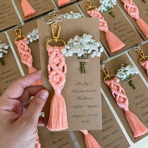 Macrame key chain knitted with cotton rope is attached to a personalized kraft card. There are white flowers on the card.