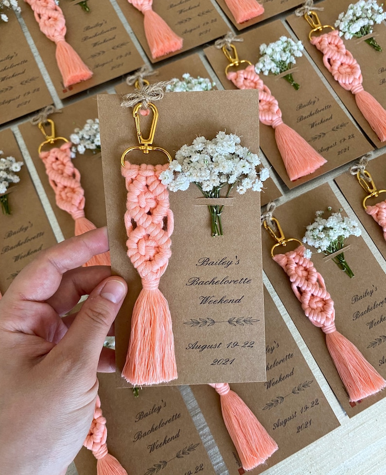 Macrame key chain knitted with cotton rope is attached to a personalized kraft card. There are white flowers on the card.
