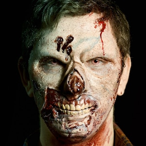 Puede incluir: Primer plano de una cara con maquillaje de zombie. El maquillaje incluye sangre falsa, una nariz deformada y una sonrisa grotesca.