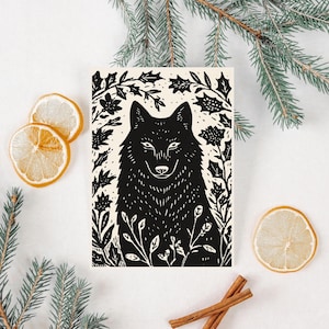 Peut inclure: Illustration en noir et blanc d'un loup entouré de feuillage. L'œuvre d'art est sur un fond crème et est encadrée par des brins de conifères, des tranches de citron séchées et des bâtons de cannelle.
