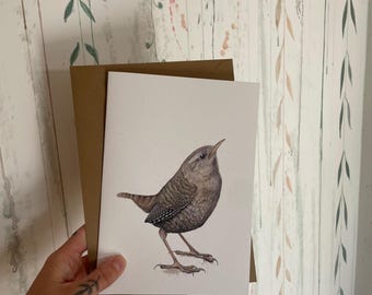 May include: A watercolor illustration of a small brown bird with detailed feather patterns, standing on a white card. The card is held with a brown envelope against a wallpaper background with a leaf design.