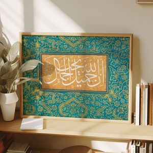 Peut inclure: Une impression encadrée de calligraphie islamique en blanc sur fond doré. La calligraphie est entourée d'une bordure bleu sarcelle avec des motifs floraux dorés. Le cadre est en bois et a une finition brun clair.