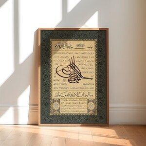 May include: A framed print of Islamic calligraphy in black and gold on a beige background. The calligraphy is surrounded by a decorative border in green and gold. The text includes the phrase "Allah" and other Arabic words.