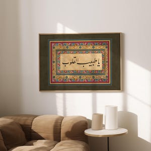 May include: A framed print of Islamic calligraphy in black ink on a gold background. The calligraphy is surrounded by a colorful floral border with intricate details. The frame is dark green.