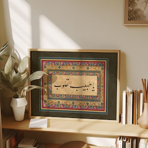 May include: A framed print of Arabic calligraphy in black ink on a beige background. The calligraphy is surrounded by a colorful floral border with red, blue, yellow, and green accents. The frame is dark green with a gold border.
