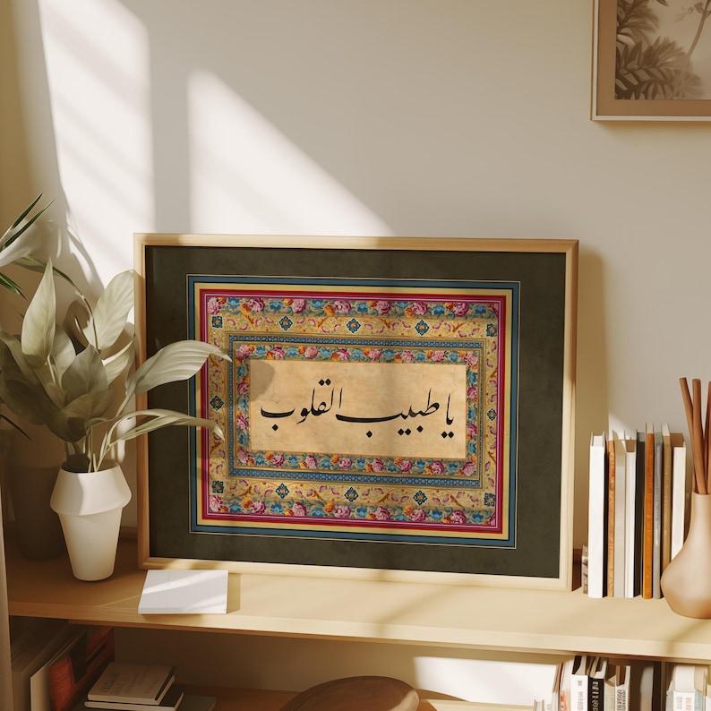 May include: A framed print of Arabic calligraphy in black ink on a beige background. The calligraphy is surrounded by a colorful floral border with red, blue, yellow, and green accents. The frame is dark green with a gold border.