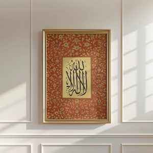 Puede incluir: Una impresión enmarcada de caligrafía islámica en tinta negra sobre fondo crema. La caligrafía está rodeada de un patrón floral rojo y dorado. El marco es dorado.