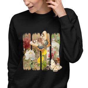 May include: Black sweatshirt featuring a colorful butterfly and floral design. The graphic includes a butterfly with orange, brown, and yellow wings, and various flowers. The design is printed on a black, long-sleeved sweatshirt.