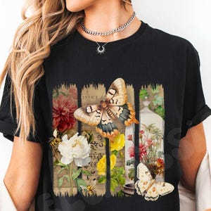 May include: Black t-shirt featuring a colorful butterfly and floral design. The graphic includes a large butterfly with detailed wing patterns, flowers, and the word "BLACK" at the bottom. The design is printed on a black t-shirt.