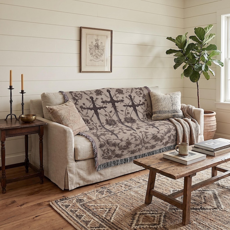 a cozy living room with a beige sofa adorned with a patterned throw blanket, a wooden coffee table, and a framed picture on the wall. The room is decorated with a potted plant, a candle holder, and a book, creating a warm and inviting atmosphere.