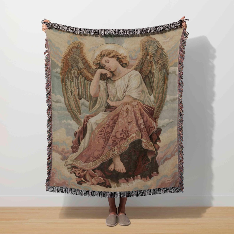 A person is holding a large tapestry featuring an angel with wings and a halo, standing on a wooden floor against a white wall.
