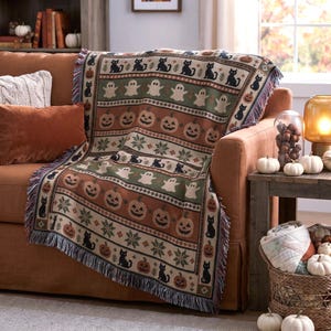 a cozy living room with a brown couch, a decorative throw blanket with Halloween-themed patterns, and a basket of pumpkins on a side table.