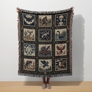 Peut inclure: Une couverture tissée avec un motif répété de créatures mythiques et de cryptides, dont Bigfoot, un phénix et un griffon. La couverture a un fond noir avec une bordure décorative et des franges.