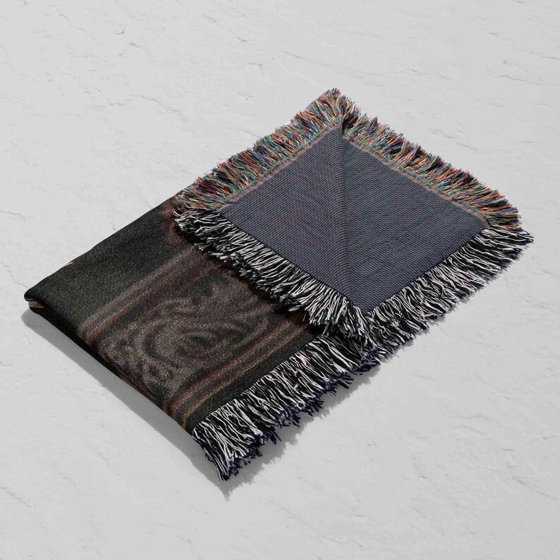 a black and gray blanket with fringed edges, folded in half and placed on a white surface.