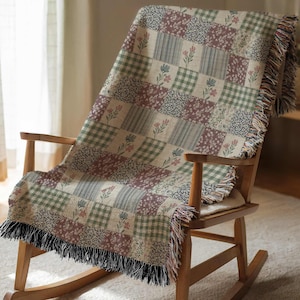 May include: A patchwork throw blanket draped over a wooden rocking chair. The blanket features squares of floral, striped, and checkered patterns in shades of green, mauve, and cream. The edges are finished with a fringe.