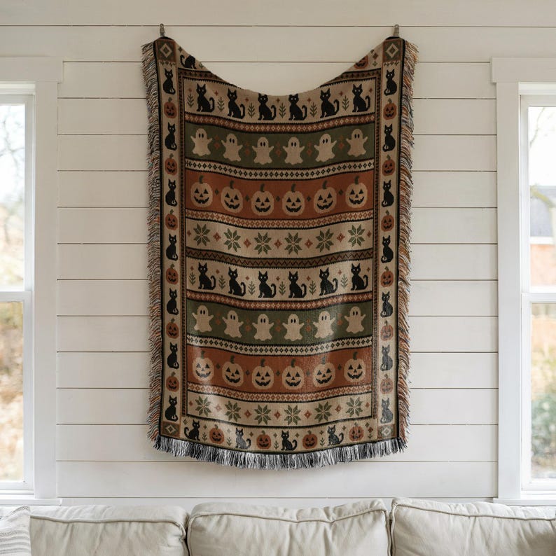 Woven blanket with Halloween theme: black cats, pumpkins, and ghosts.