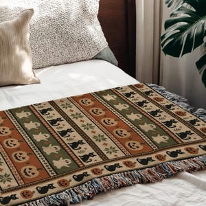 Knit blanket with Halloween patterns: pumpkins, black cats, ghosts, and snowflakes.