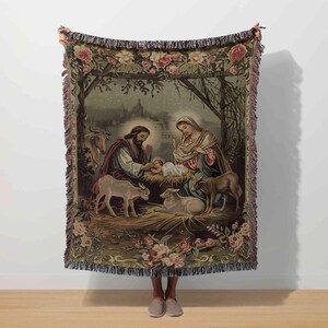 May include: A tapestry throw blanket depicting a Nativity scene with Mary, Joseph, and baby Jesus. The blanket has a floral border with pink roses and a fringed edge. The artwork shows animals and a starry night scene.