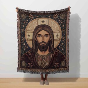 May include: A tapestry throw blanket featuring a portrait of Jesus Christ with a halo and long hair. The blanket has a dark blue background with floral and geometric patterns, and a fringed edge. The portrait is centered on the blanket.