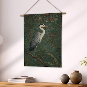 May include: A wall hanging featuring a detailed illustration of a heron perched on a branch. The bird has gray and white feathers and a long orange beak. The background is a dark green tapestry with floral and leaf patterns, creating a nature-inspired aesthetic.