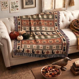 a cozy living room with a white sofa, a decorative Halloween-themed blanket, and various fall-themed decor items such as pumpkins, a bird figurine, and a bowl of autumn leaves.