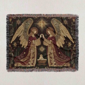 The image is a tapestry or blanket featuring two angels with wings, one on each side, standing in front of a baby Jesus. The angels are depicted in a decorative and ornate style, with intricate patterns and designs. The background of the tapestry is dark, with stars and a sun shining brightly, creating a festive and celebratory atmosphere.