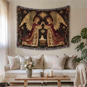a living room with a large tapestry hanging on the wall above a white sofa. The tapestry depicts two angels with wings, one on each side, standing in front of a baby in a crib. The room also includes a coffee table with a vase of flowers, a book, and a candle.