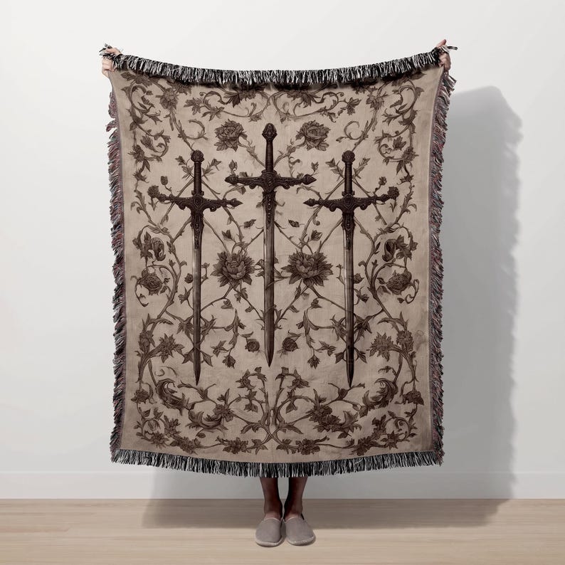 A person is holding up a large blanket with a floral design and three crossed swords on it.