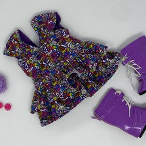 K&ouml;nnte beinhalten: Ein Puppen-Outfit mit einem farbenfrohen gemusterten Kleid, lila Stiefeln mit wei&szlig;en Schn&uuml;rsenkeln, einem lila Pompon und rosa bl&uuml;tenf&ouml;rmigen Ohrringen. Das Kleid hat einen lebendigen Druck mit verschiedenen Formen und Farben.