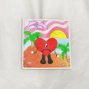May include: Embroidered patch featuring a red heart character with a sad expression, black legs, and white hands. The patch depicts a beach scene with palm trees, dolphins, a sunset, and flowers. The patch is square with a white border.