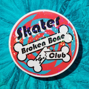 May include: A round sticker with a red and blue swirl design. The sticker says "Skater Broken Bone Club" in black text with white bone graphics.