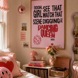 Puede incluir: Un póster de pared enmarcado con fondo rosa claro que presenta texto en negro y rojo que dice: OOOH, SEE THAT GIRL WATCH THAT SCENE DIGGING THE DANCING QUEEN ABBA. El póster incluye un gráfico de una bola de discoteca rosa en la pared.