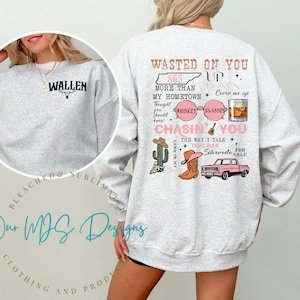 Könnte beinhalten: Grauer Pullover mit einem Country-Musik-Design. Der Text auf dem Pullover lautet "Wasted on You", "865 More Than My Hometown", "Up Down", "Cover Me Up", "Whiskey Glasses", "Chasin' You", "The Way I Talk", "This Bar", "For Silverado Sale".