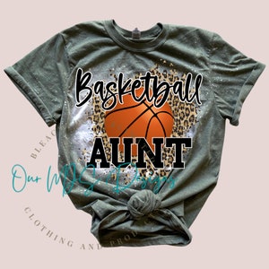 May include: Green t-shirt with a distressed design featuring a basketball and the text "Basketball Aunt" in black.