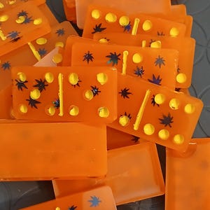 May include: A collection of orange dominoes with yellow dots and decorative blue and green accents. The dominoes are rectangular and appear to be made of a translucent material. The image shows a close-up view of the game pieces.