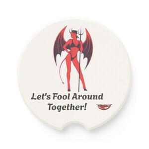 May include: A round white car coaster featuring a red devil graphic with black wings and a pitchfork. Below the figure, the text reads "Let's Fool Around Together!" accompanied by a small illustration of red lips. The coaster has a notched edge.