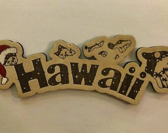 May include: Wooden Hawaii magnet with a Santa hat and tropical island illustrations. The word "Hawaii" is in dark brown, with a light brown background and white accents. A festive souvenir.