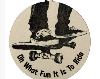 May include: A circular, off-white graphic features a black and white illustration of a skateboard with a person's legs and feet on top. The text "Oh What Fun It Is To Ride" is printed around the bottom edge.