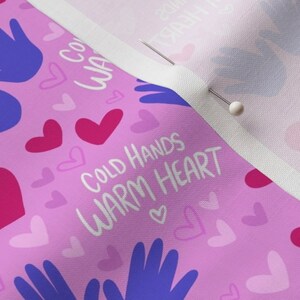 May include: Pink fabric with a repeating pattern of blue hands, pink hearts, and white hearts. The text "COLD HANDS WARM HEART" is written in white.