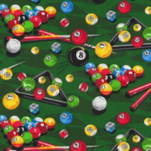 May include: A green felt pool table with a variety of billiard balls in red, yellow, blue, and white. The balls are arranged in a random pattern on the table, with some balls in the pockets. There are also two pool cues and a triangle rack on the table.